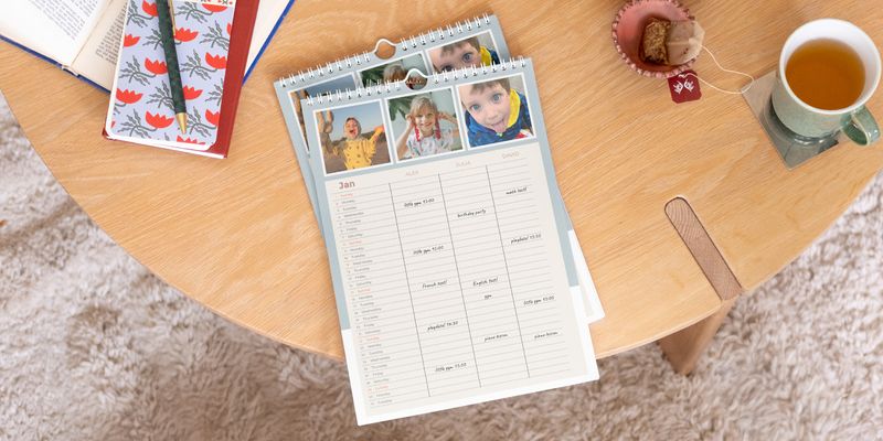 Personalisierter posterXXL Familienplaner, der prominent auf einem Holztisch präsentiert wird.